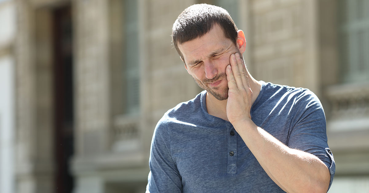 Man suffering from TMJ disorder  holding his jaw to help with the pain