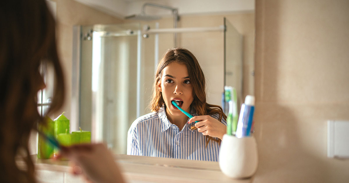 Woman looking in the mirror while brushing her teeth