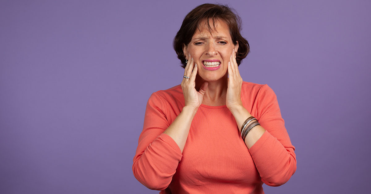 Woman applying pressure to her jaw to help alleviate TMJ pain