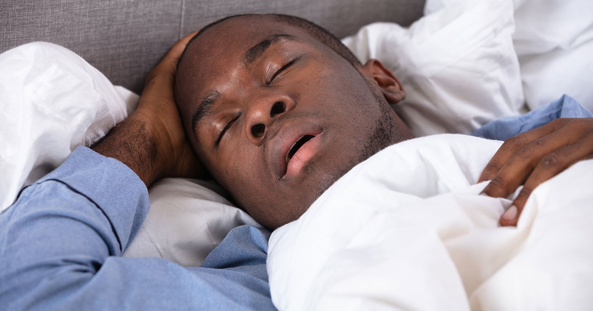 Young snoring man asleep in his bed