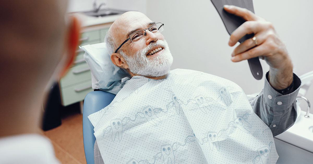 Man in a dentist chair looks at his new implant in a hand mirror