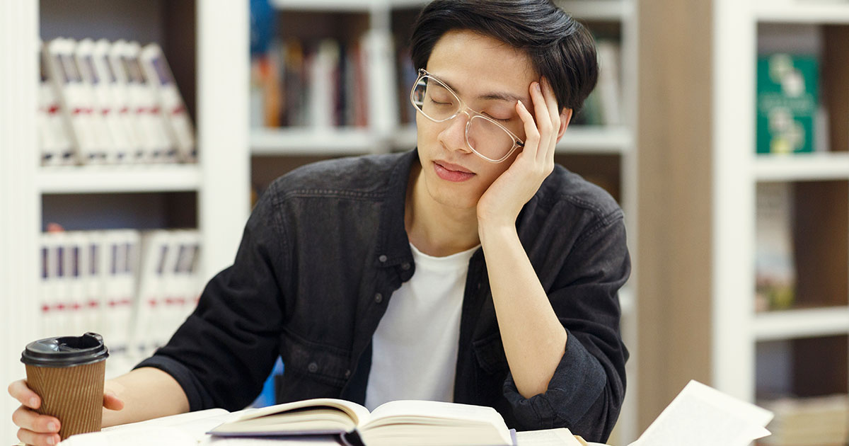 Graduate student falling asleep while studying in library, even after drinking a coffee
