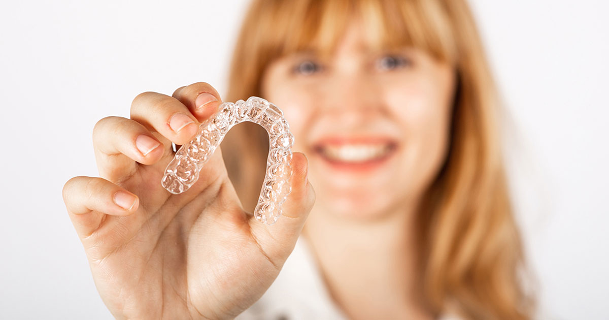 Photograph of a smiling patient holding her clear mouthguard forward in front of her.