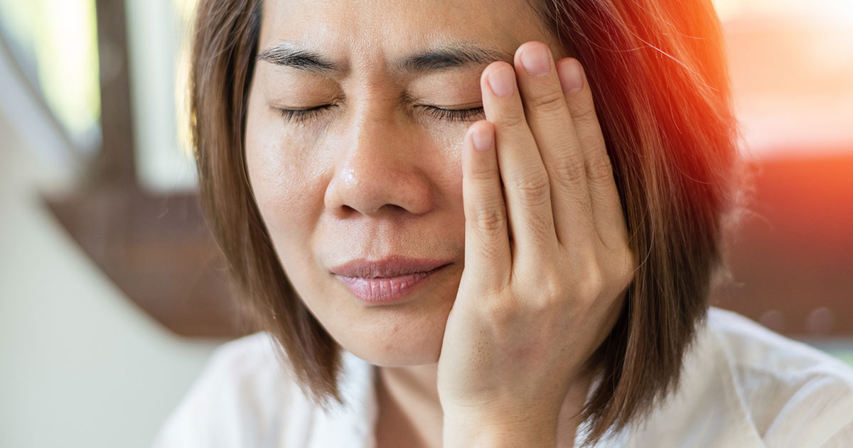 Woman holding her cheek trying to alleviate the pain caused by a sudden TMJ flare-up
