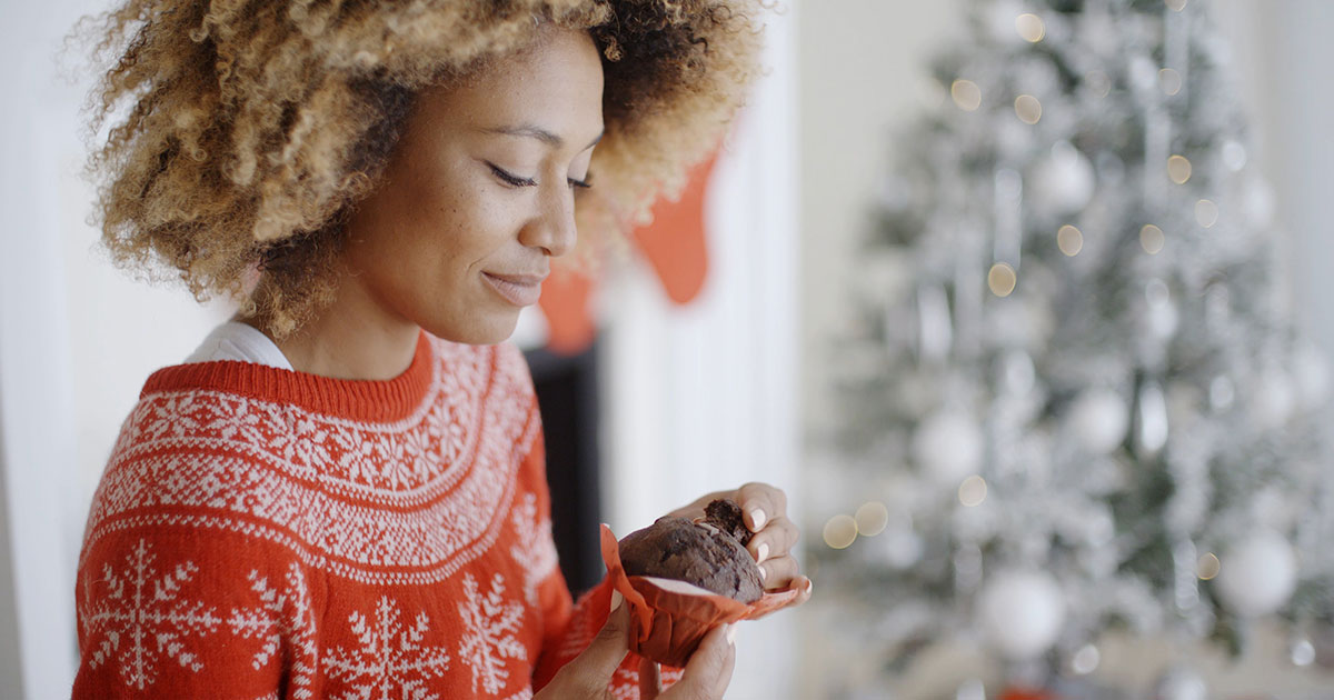 a person in a holiday sweater eating a cupcake.